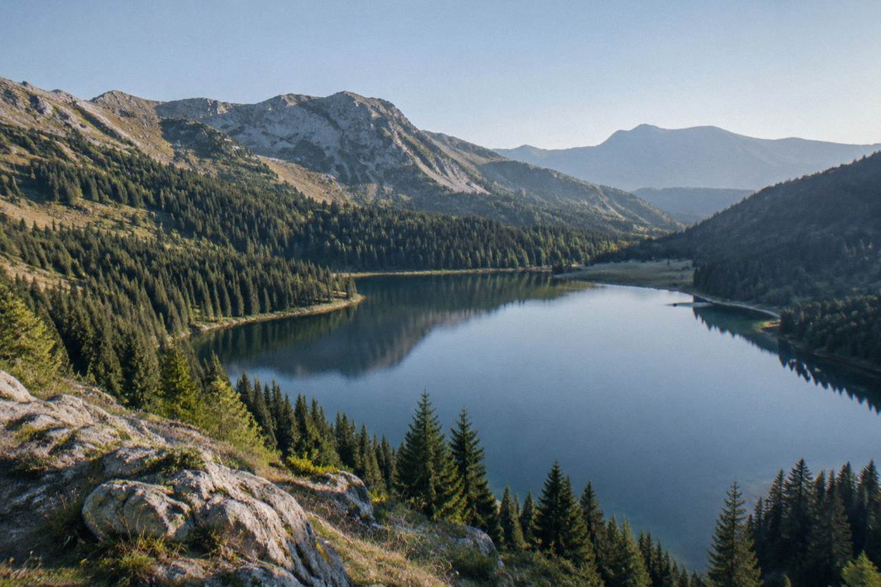 A mountain lake surrounded by forested slopes under a clear sky