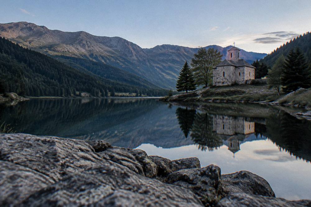 A small stone church reflected in still water at dusk