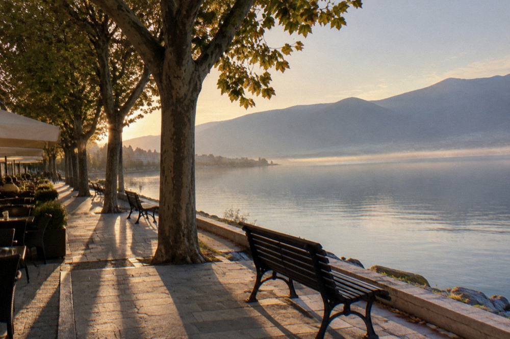A calm lake at dawn with mist over the water and a shoreline road