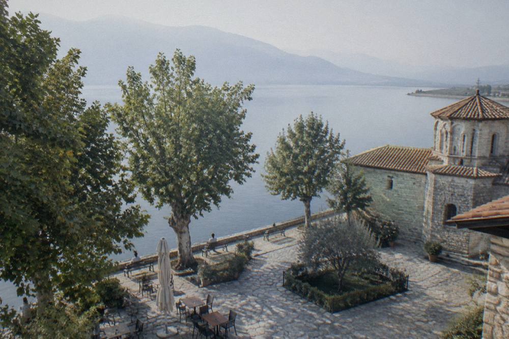 A monastery courtyard beside a lake with plane trees and still water