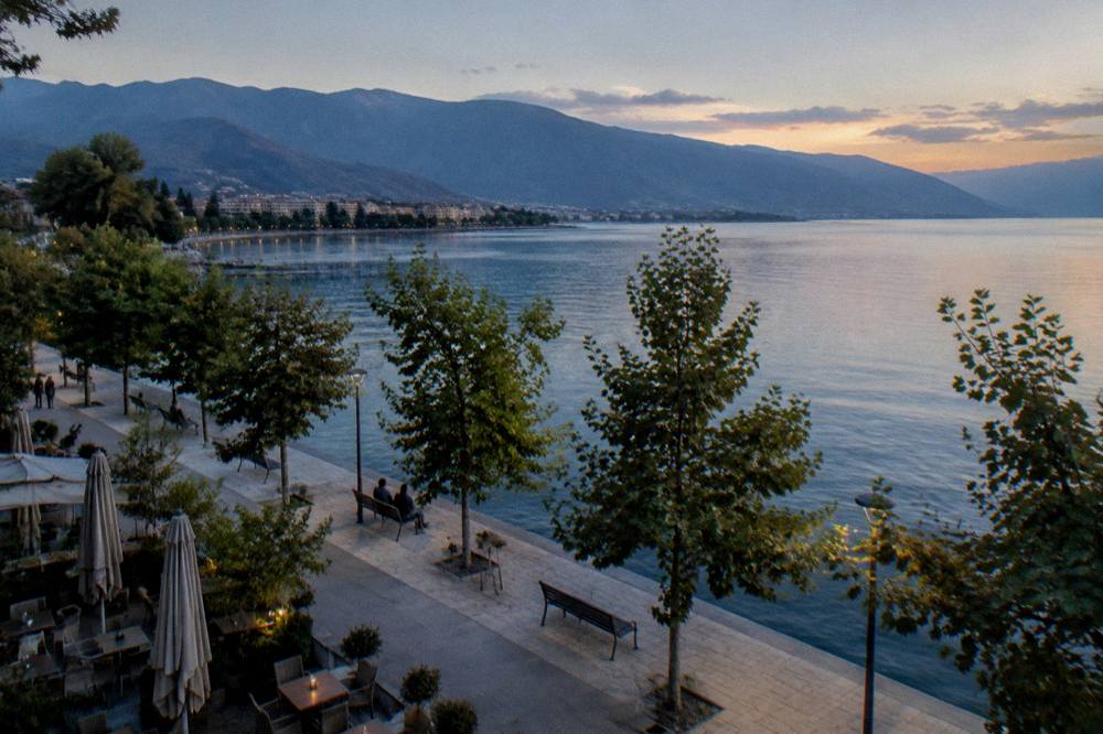 A wide view across a mountain lake toward a distant shoreline town at golden hour