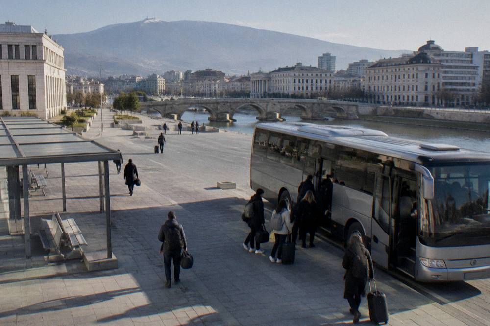 Travellers boarding an intercity bus at a station forecourt with bags