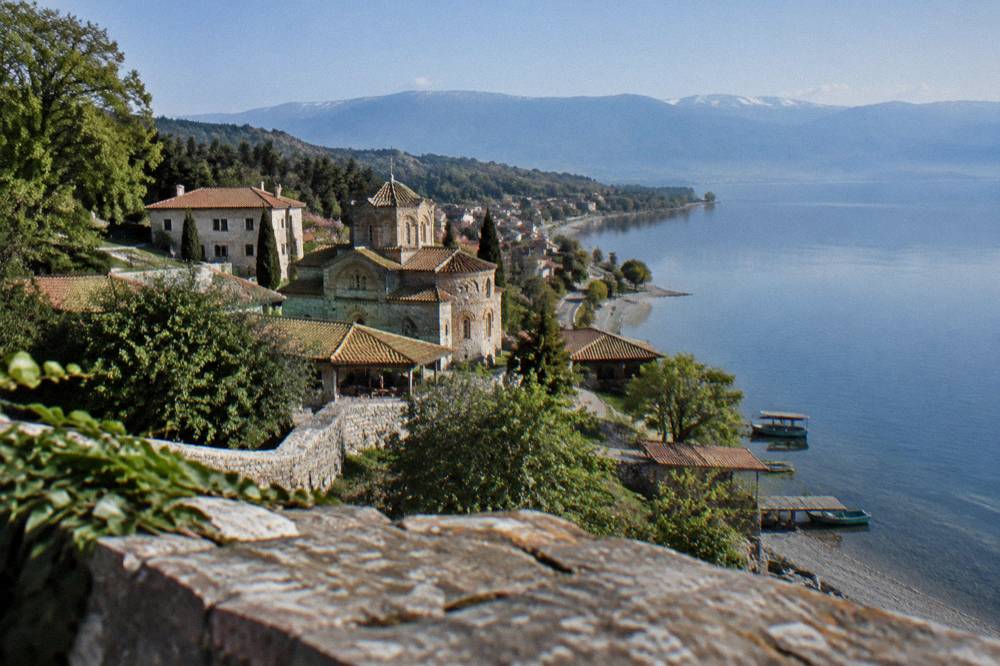 A winding road along a lakeshore with a village and pebble beach below