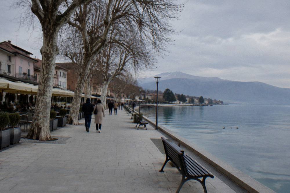 Walkers on a flat promenade beside Lake Ohrid at Struga in late afternoon light
