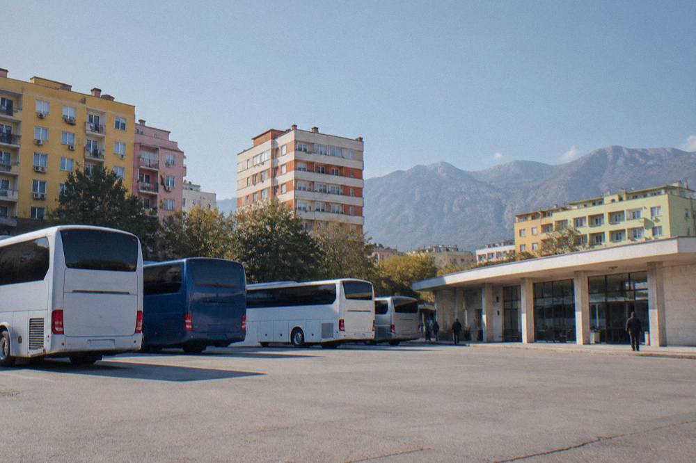 A row of parked intercity buses at a small station building in daylight