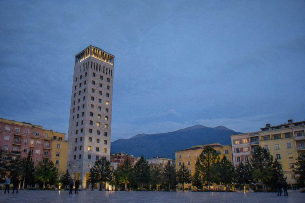 A large city square with a tall tower and pastel buildings under a blue sky