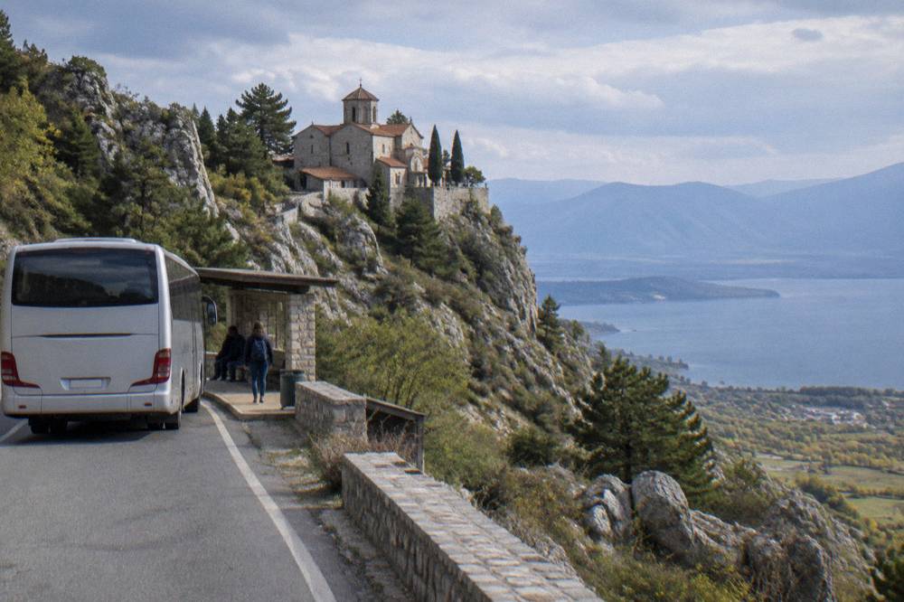A bus waiting at a small station platform beside a hillside road