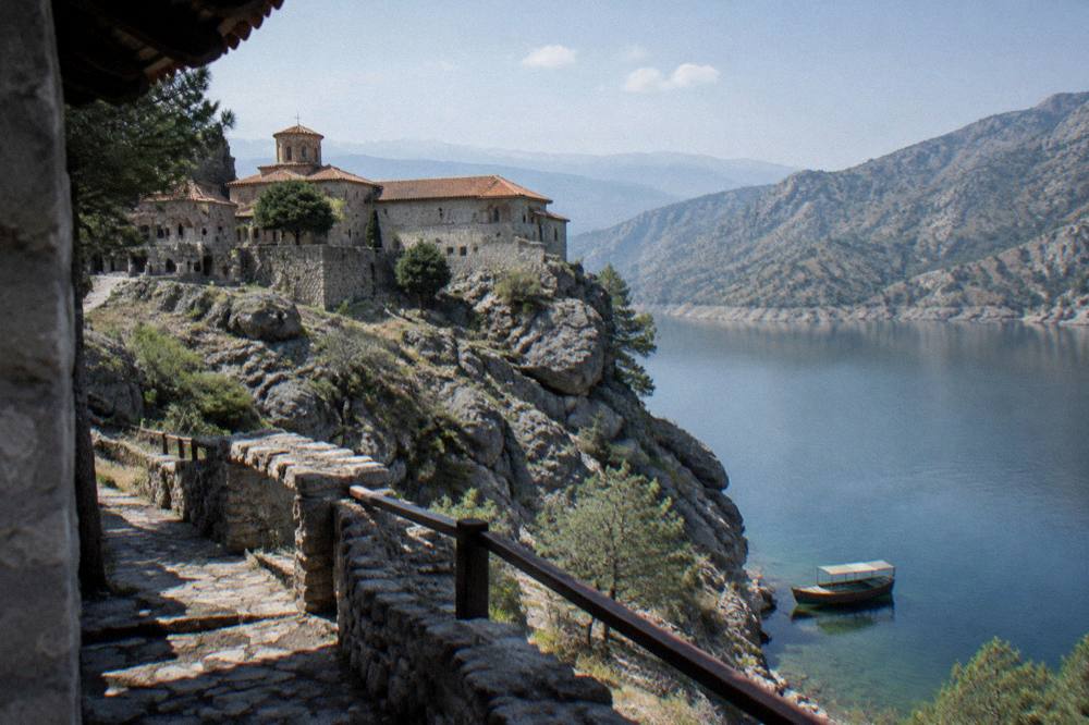 A wooden boat moored on clear green water below tall hills
