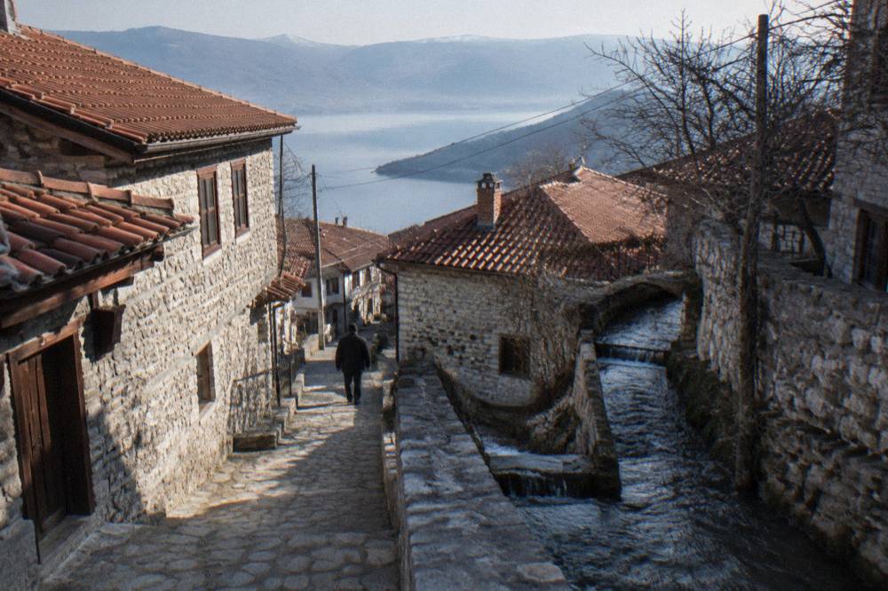 A narrow village lane of stone houses climbing a slope with the stream alongside