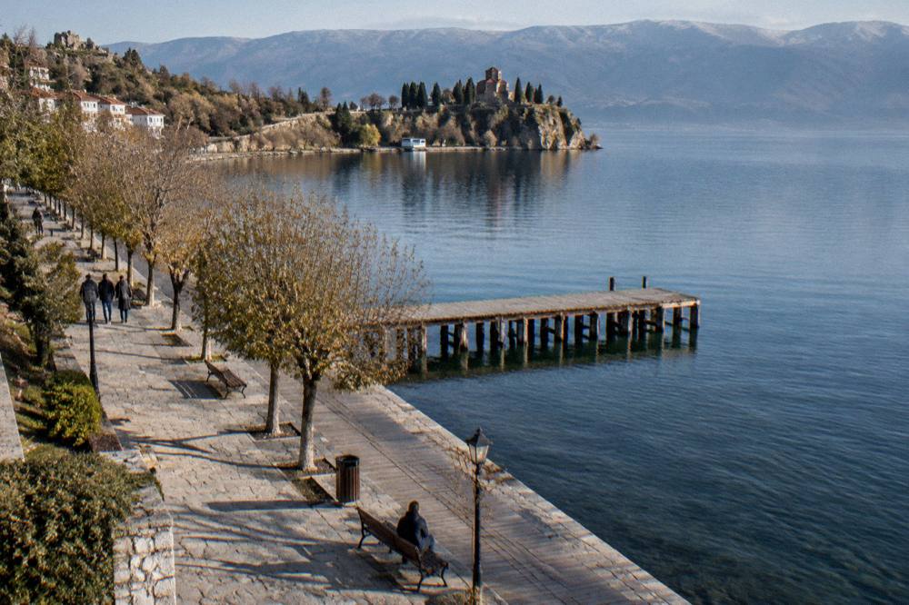 A wooden pier on a blue lake with a monastery building on the far shore