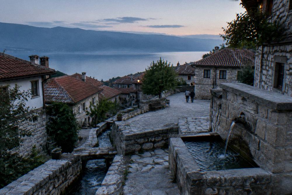 A stone fountain with clear water running into a basin at the edge of a village square