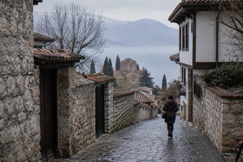 A quiet old town lane in Ohrid with stone walls and a glimpse of the lake between buildings