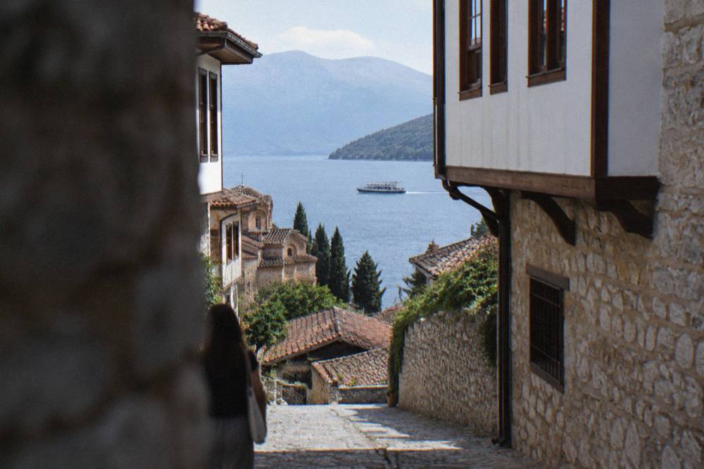 A tour boat cutting across open water on Lake Ohrid toward forested hills