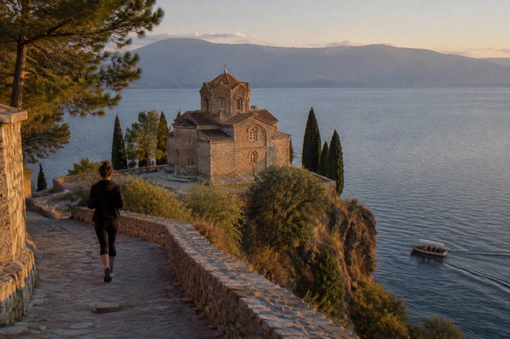 A small boat passing below the cliff-top church of St John at Kaneo at dusk