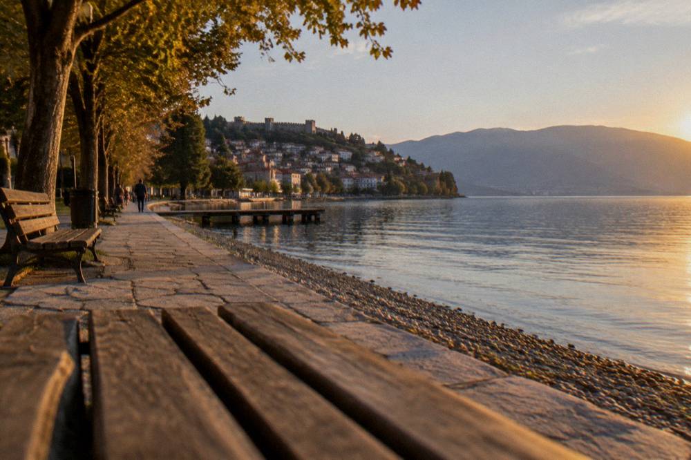 A pebble beach on a lake shore with clear shallow water and wooded hills behind