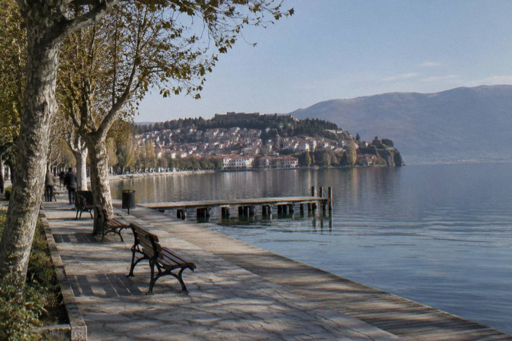 A calm lake at dusk with a town's lights beginning to show along the shore