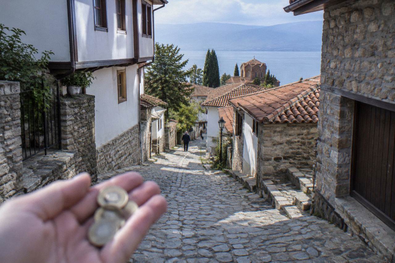 Fingers holding a few small coins above a worn stone street in Ohrid's old town