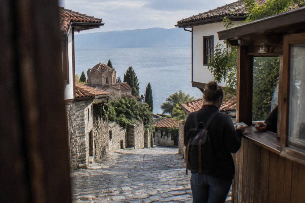 A visitor paying denar banknotes at a wooden ticket counter beside Lake Ohrid