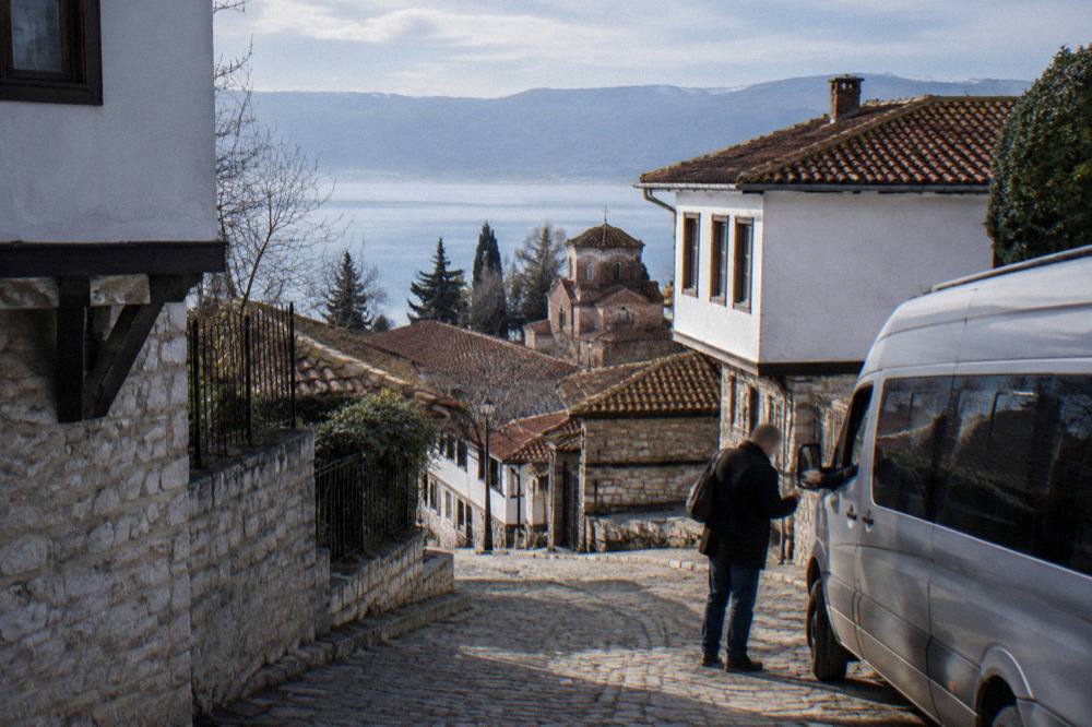 A passenger handing denar notes to a driver beside a minibus near Ohrid's lakefront