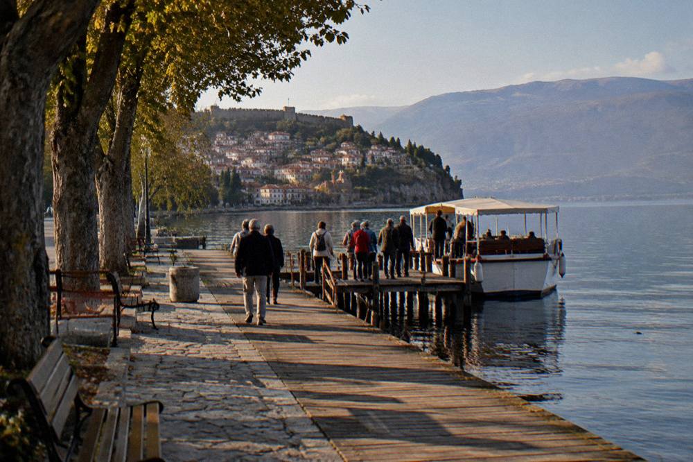 A tour group boarding a small boat at a wooden pier on Lake Ohrid