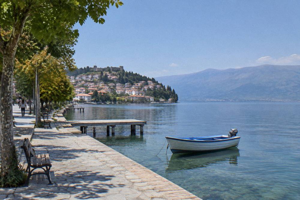 A boat moored on clear green water near the Ohrid lakeside promenade in the morning
