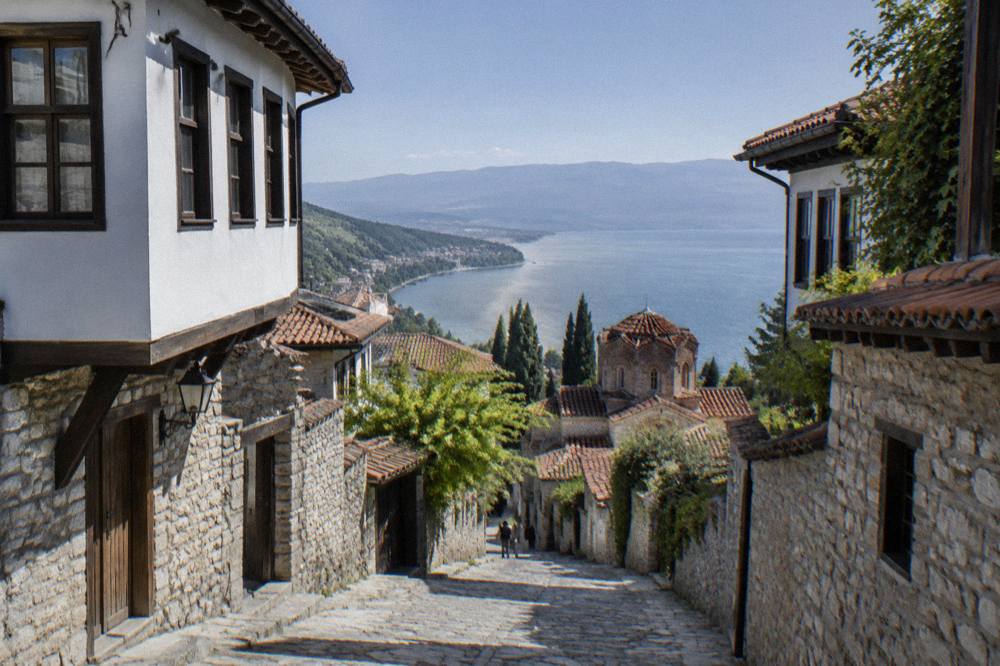 The shoreline of Lake Ohrid curving toward forested hills under a clear sky