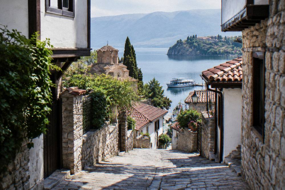 A passenger boat moored on Lake Ohrid with monastery buildings and hills beyond