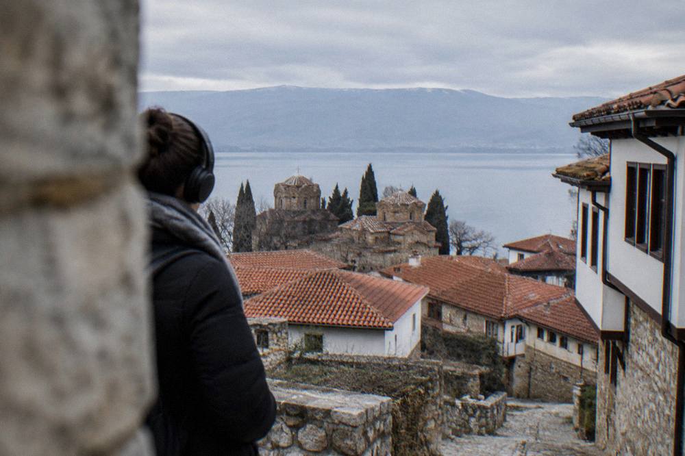 A visitor with headphones standing at a viewpoint above the red rooftops of Ohrid