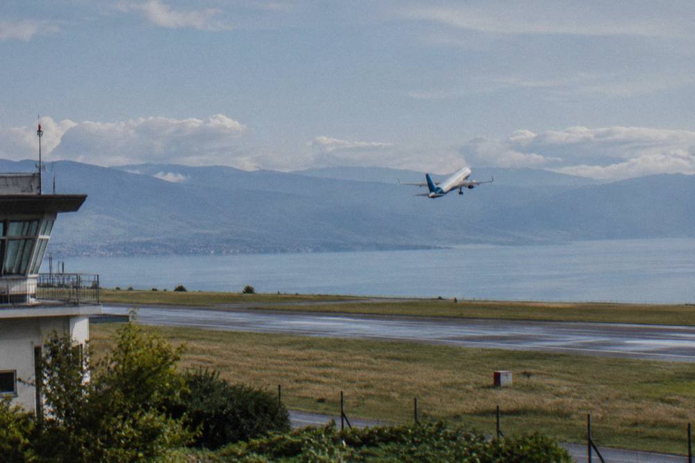 A low-cost airliner climbing away from a runway with a blue lake and hills beyond