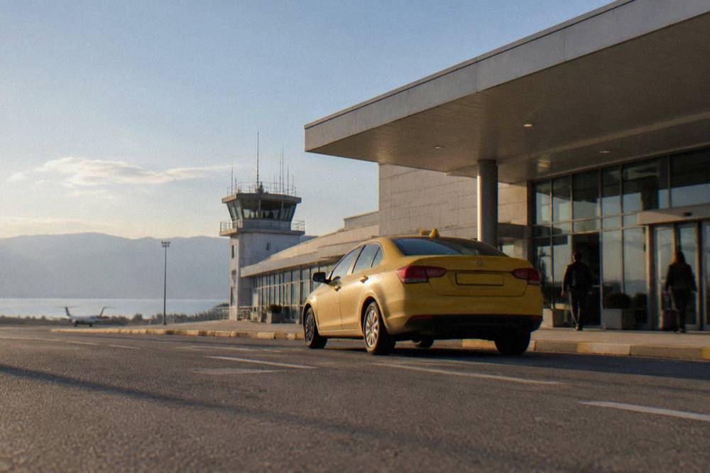 A taxi waiting outside a small airport terminal entrance on a sunny afternoon