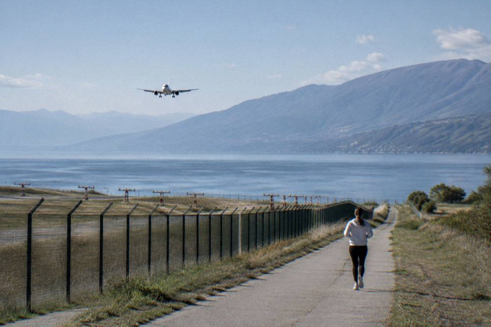 An airliner on approach over a wide blue lake surrounded by mountains
