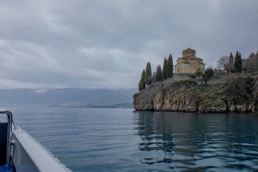 A stone church on a cliff above a blue lake seen from a boat