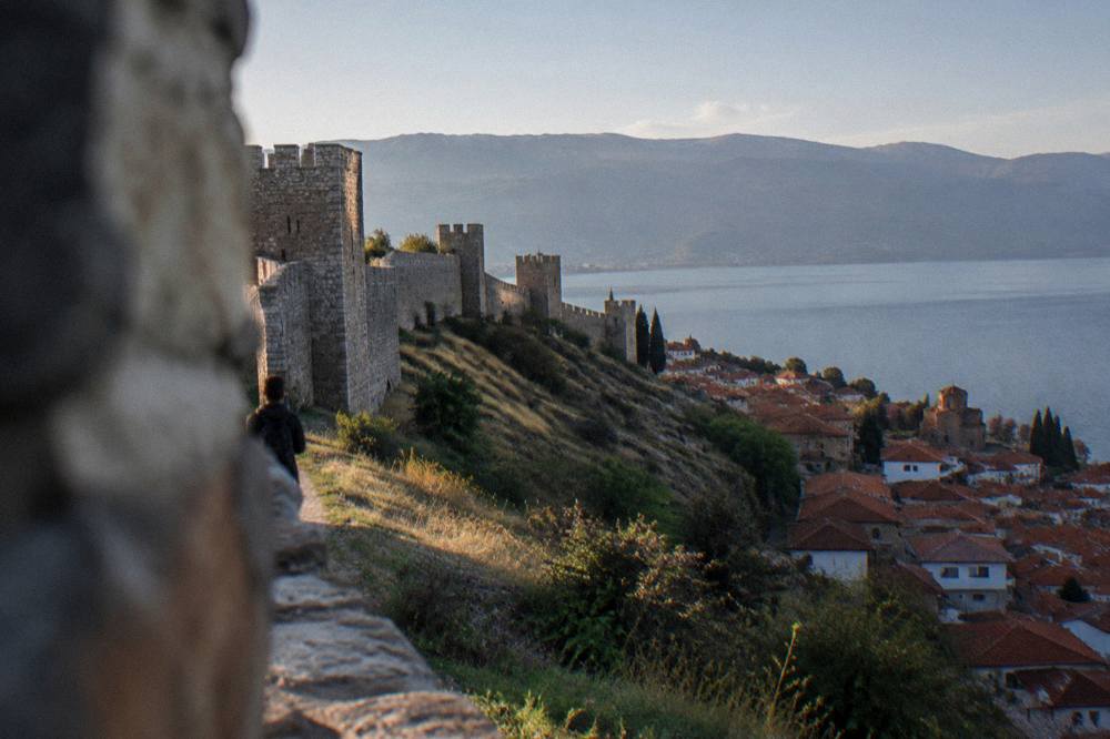 An evening view across a lake town with a fortress wall above tiled roofs