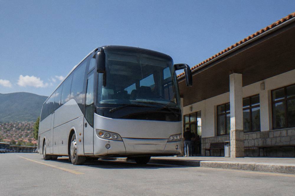 A regional coach waiting at a platform beside a simple station building under a blue sky
