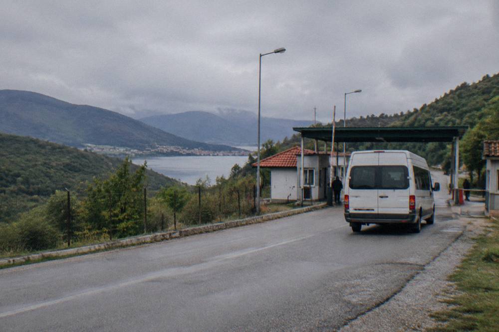 A minibus on a rural road near a small border checkpoint between green hills