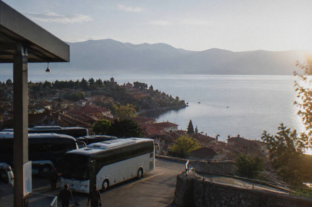 A view over red rooftops of an old lakeside town toward a wide blue mountain lake