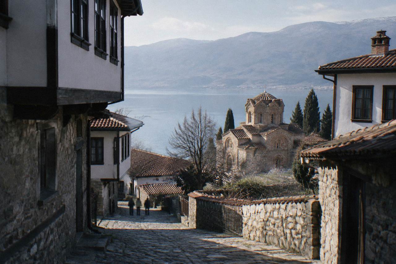 Stone church above the shoreline of a mountain lake with old town rooftops behind it