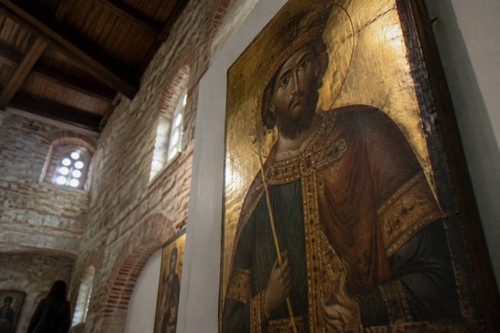 Painted wooden icon of a saint with a gold background displayed in a gallery interior