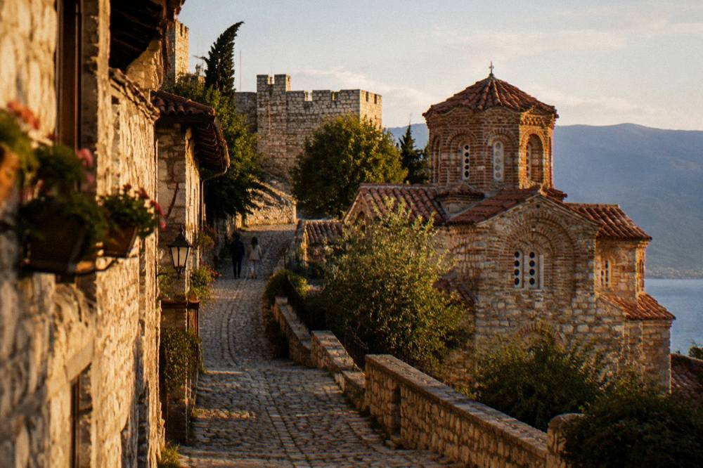 Narrow cobbled lane between old stone houses climbing toward a stone fortress wall