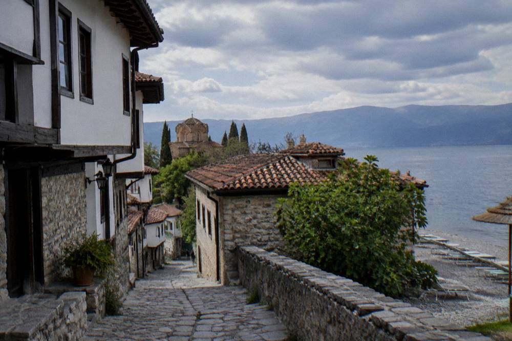Empty sun loungers on a pebble beach beside Lake Ohrid under an overcast sky