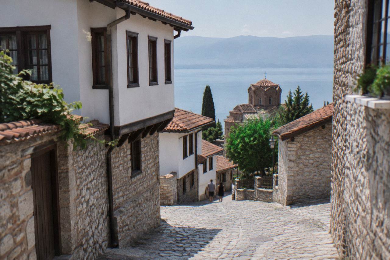 A narrow stone lane in Ohrid old town with whitewashed houses and a church tower above the lake