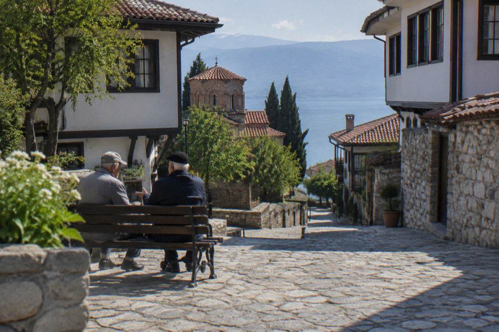 Two older men talking on a bench in a sunny square in Ohrid