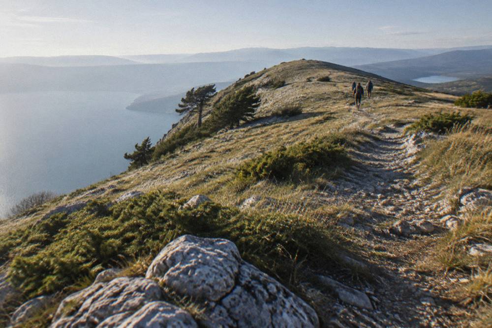 A marked mountain path crossing open grassland on a high ridge with two lakes in the far distance
