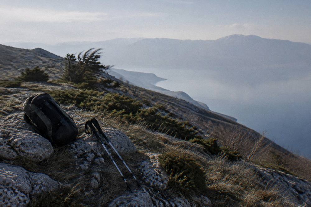 A backpack and walking poles resting on a rock beside the lake shore in morning light