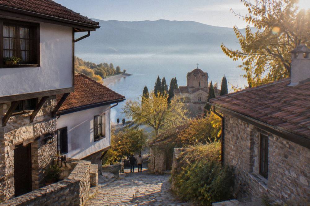 A pebble beach on Lake Ohrid with calm water and autumn trees along the shore