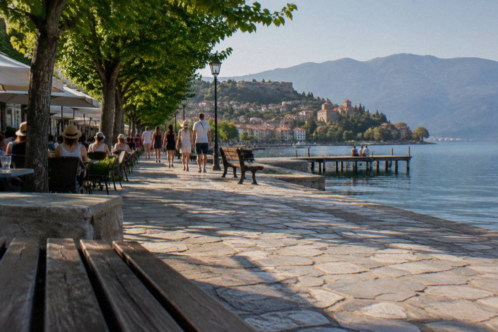 A busy lakeside promenade in Ohrid with people strolling among cafe tables in the evening
