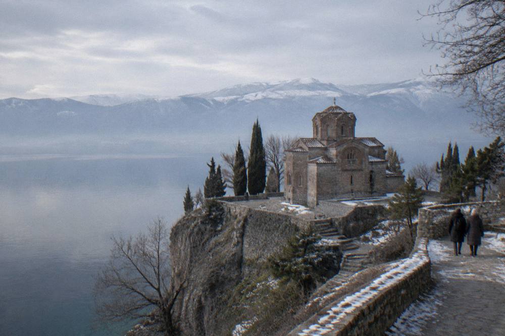 Church of St John at Kaneo above a still winter lake with snow-dusted hills behind