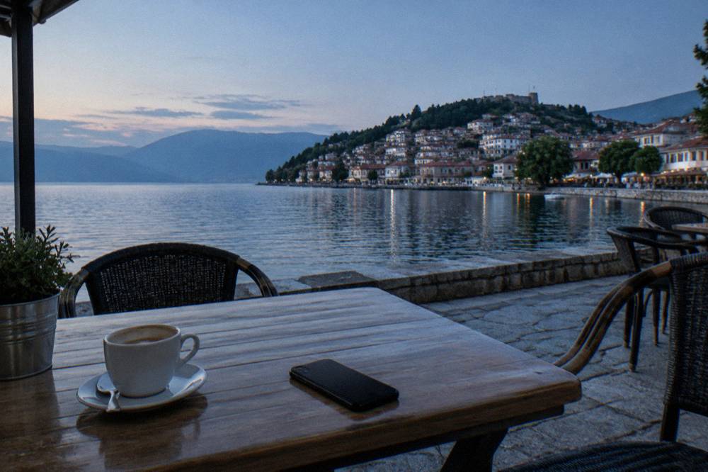 A lakeside cafe table in Ohrid with a coffee cup and a closed phone lying face down, the lake behind