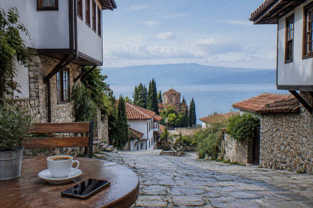 A lakeside cafe table in Ohrid with a phone and a coffee beside the water