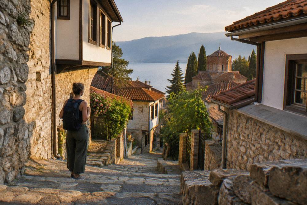 A woman with a backpack pausing on a stone stairway between old houses in Ohrid